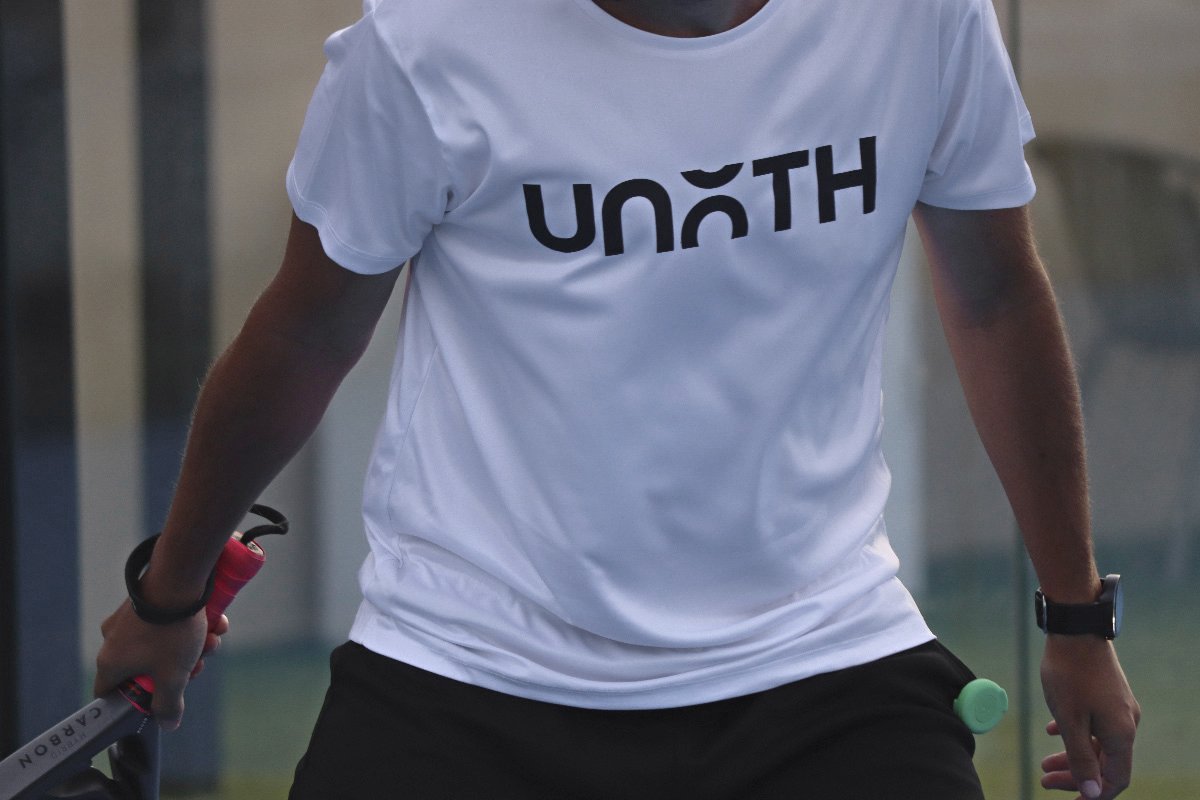 Jugador de pádel con camiseta Unoth sosteniendo pulsador verde en pista